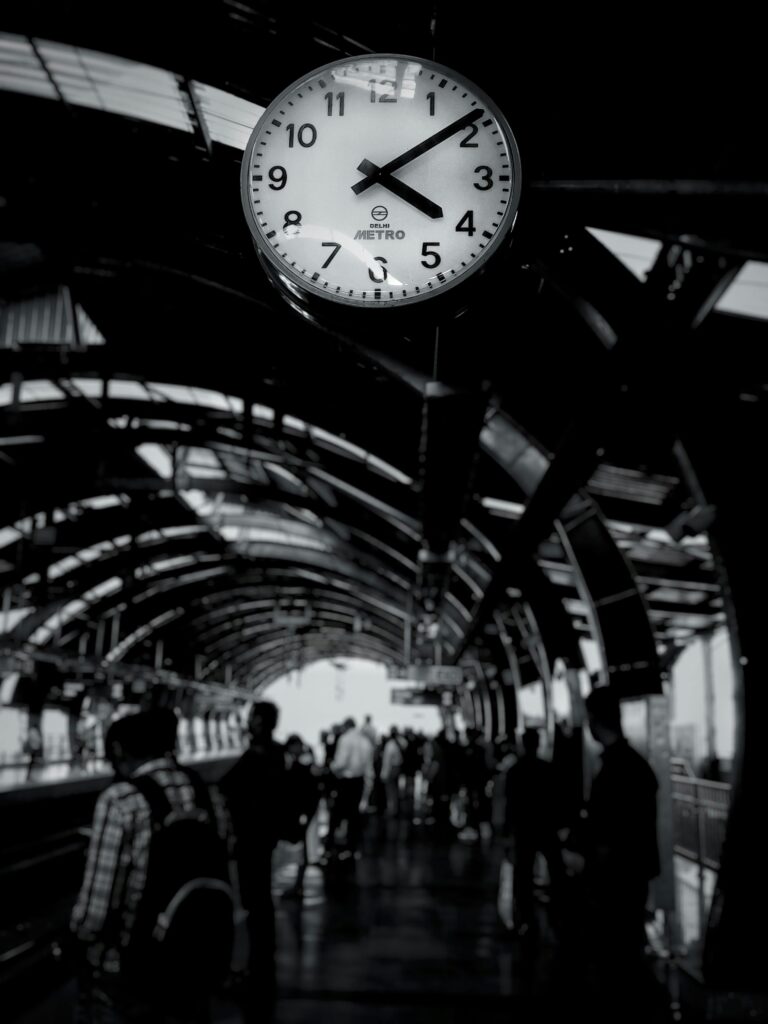 Black and white photo of a bustling metro station with a prominent clock and commuters.